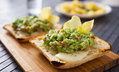 toasted slices of square bread with warm cheese and homemade guacamole on plate for healthy...