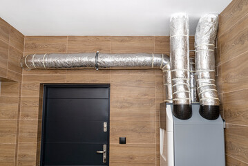 Home mechanical ventilation with heat recovery hanging on the wall in a modern gas boiler room with...