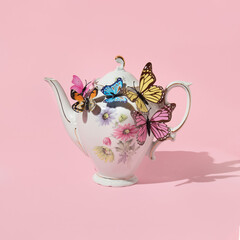 Spring creative layout with english garden teapot with colorful butterflies on pastel pink background. 80s, 90s retro romantic aesthetic summer concept. Minimal surreal fashion tea idea.