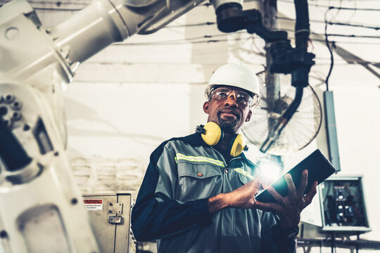 African American factory worker working with adept robotic arm in a workshop . Industry robot programming software for automated manufacturing technology .