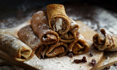 Rolled up pancakes with cottage cheese and raisins on wooden stand with flour