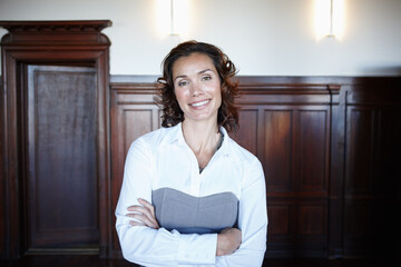 Ready for the judge. Attractive female legal person standing with her arms folded and smiling widely in the courtroom.