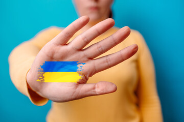Stop war. Woman shows a palm with ukraine flag on hand in camera isolated on blue background