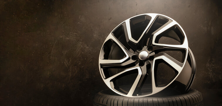 new stylish cool alloy wheel on the tire dark textured background, beautiful and expensive 20 -21, 22 ,large diameter copy space on the left