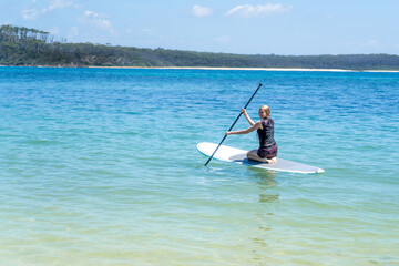 Girl wearing rash guard on a stand-up paddle board at the ocean bay in Australia. SUP water sport activity