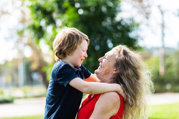 Grandmother carrying her grandson, laughing together outside at a park