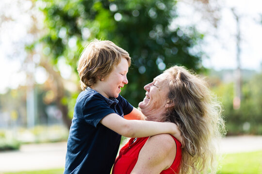 Grandmother carrying her grandson, laughing together outside at a park