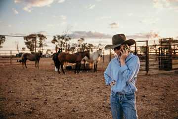 teenager standing near horses talking on her mobile