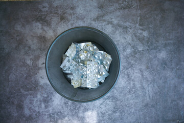 top view of pills and blister packs in a bin on black background 