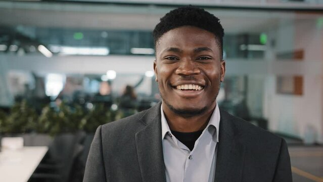 Young man millennial American African businessman team leader office general manager in profile posing turning satisfied confident looking at camera with dental smile standing close view male portrait