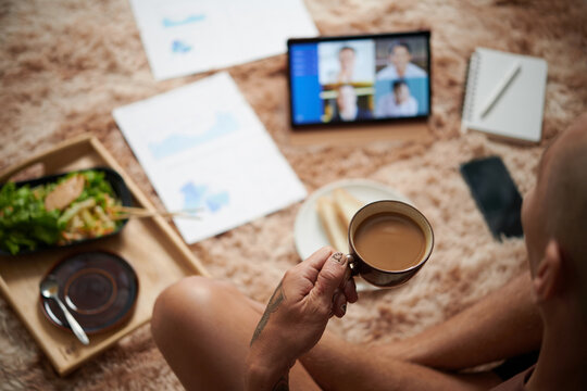 Man drinking cup of morning coffee when having online meeting wth colleagues, working from home concept