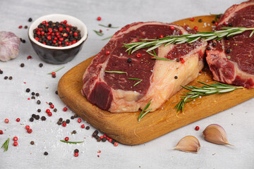 Raw beef steak on a cutting board with rosemary and spices.