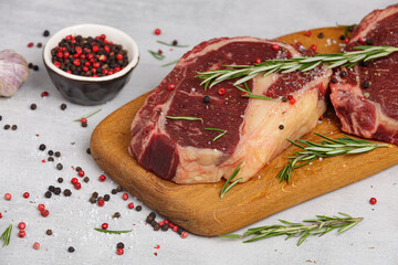 Raw beef steak, dry aged T bone with red hot pepper and spices on black cutting board background,...