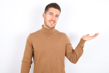 Fototapeta premium young caucasian man wearing grey turtleneck over white background smiling cheerful presenting and pointing with palm of hand looking at the camera.