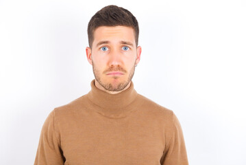 Displeased upset young caucasian man wearing grey turtleneck over white background frowns face as going to cry, being discontent and unhappy as can't achieve goals,  Disappointed model has troubles