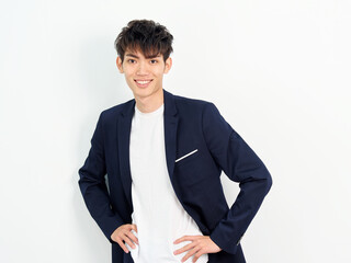 Portrait of handsome Chinese young man in dark blue leisure suit posing against white wall...