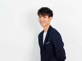 Portrait of handsome Chinese young man in dark blue leisure suit posing against white wall background. Arms on back and looking at camera, looks confident, side view.