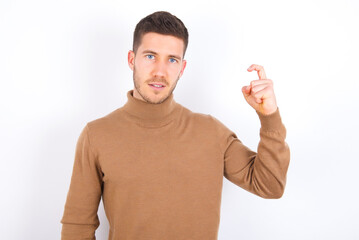 young caucasian man wearing grey turtleneck over white background pointing up with fingers number...