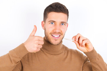 young caucasian man wearing grey turtleneck over white background holding an invisible braces...