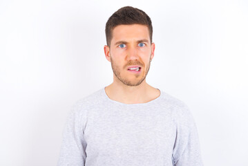 Portrait of dissatisfied young caucasian man wearing grey sweater over white background smirks...