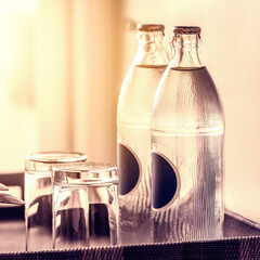 two bottles of mineral water in the hotel room, as well as clean glasses on a tray, light from the...