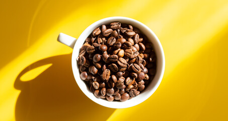 Coffee beans in a white ceramic cup on a yellow background. Hard sun shadows. Top view