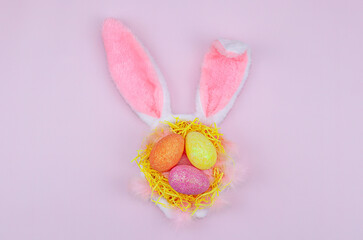 Colored Easter eggs lie in the ears of a carnival rabbit on a pink background. Flat lay.