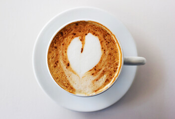 The best start to any morning. A freshly-made cappuccino on a white table with a heart shape in the milk froth.