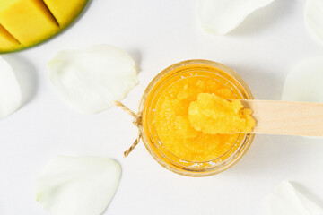 Cosmetic scrub made from sugar and ripe mango on a white wooden table, top view.