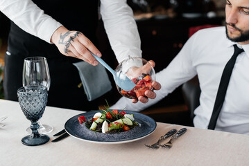 The waiter makes an exquisite serving of seafood salad, tuna and black caviar in a beautiful serving on the table in the restaurant. Exquisite delicacies of haute cuisine close-up.