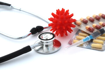 On a white background lies a stethoscope, pills, a syringe and a mock-up of the virus.