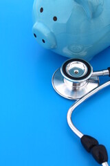 On a blue background lies a stethoscope and a piggy bank.