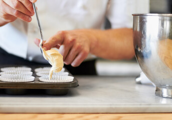 Batter up. A close up of a baker pushing cupcake batter from a spoon into the cupcake tray.