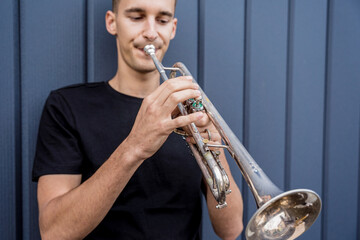 Young street musician playing the trumpet near the big blue wall