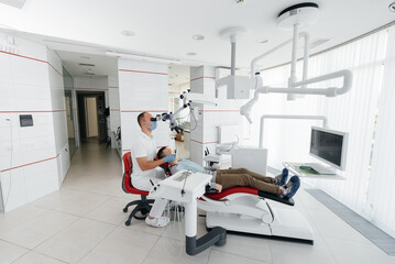 A young dentist examines and treats the teeth of a young guy in modern white dentistry using a microscope. Dental prosthetics, treatment and teeth whitening. Prevention of caries.