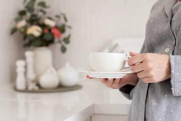 A girl in the kitchen pours boiling water into a cup in the morning. He holds a cup in his hands.
