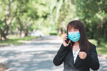 business woman wearing face mask using smartphone tablet in calling for working with her customer in park with sunrise and blur nature background. business new normal with corona virus or covid-19.