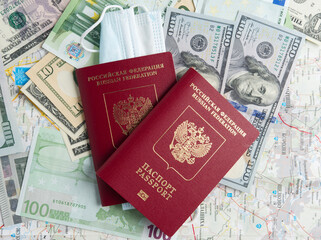 Two Russian passports are on dollar and euro bills. A medical mask is attached to one of the passports. The concept of traveling during a pandemic and diseases. Top view, flat lay