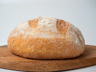 A close-up of freshly baked wheat bread with a crispy crust lies on a wooden tray. Side view,...