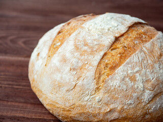 Close-up of a round loaf of wheat bread lying on a brown wooden background. Baking, bakery concept. Side view