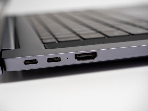Close-up of a part of a laptop standing on a light background. Large USB type S and HDMI ports on the laptop. Open laptop, keyboard, selective focus