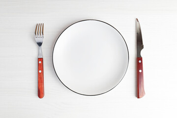 Empty white plate, fork and knife on white wooden table. Top view. Copyspace.