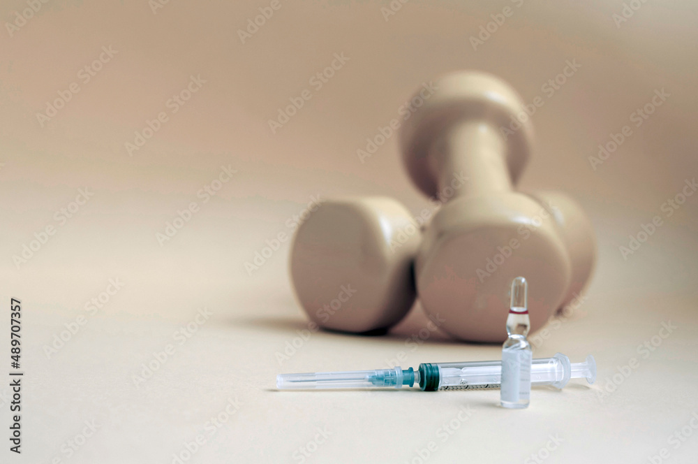 Poster syringe and a medical ampoule with liquid stands in front of dumbbells on a yellow background, copy 