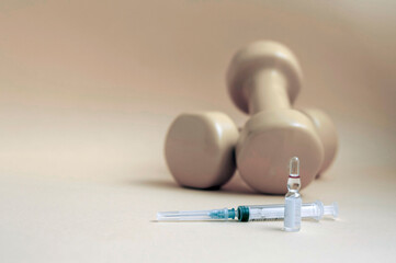 syringe and a medical ampoule with liquid stands in front of dumbbells on a yellow background, copy...