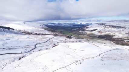 A snow-covered Scottish landscape. Aerial image of a green, quiet, Scottish glen surrounded by snow-covered hills with snow-topped mountains in the distance. A cold, tranquil mood, scene.