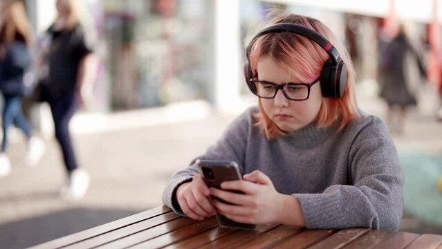 serious chubby little girl is viewing video in social media in smartphone, listening by headphones