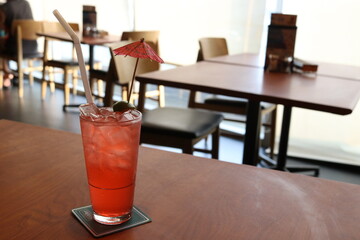 A glass of punch and ice is on brown wood table. small paper umbrella are in glass.