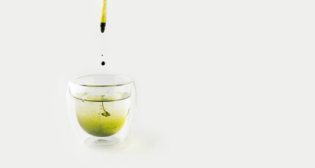 Liquid chlorophyll extract is pipetted into a glass of water. White background. The concept of...