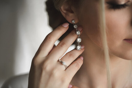 Wedding earrings on a woman's hand, she takes earrings, bride fees, morning bride, white dress, wearing earrings
