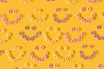 colored breakfast cereals laid out in the shape of a smiley face on a yellow background top view